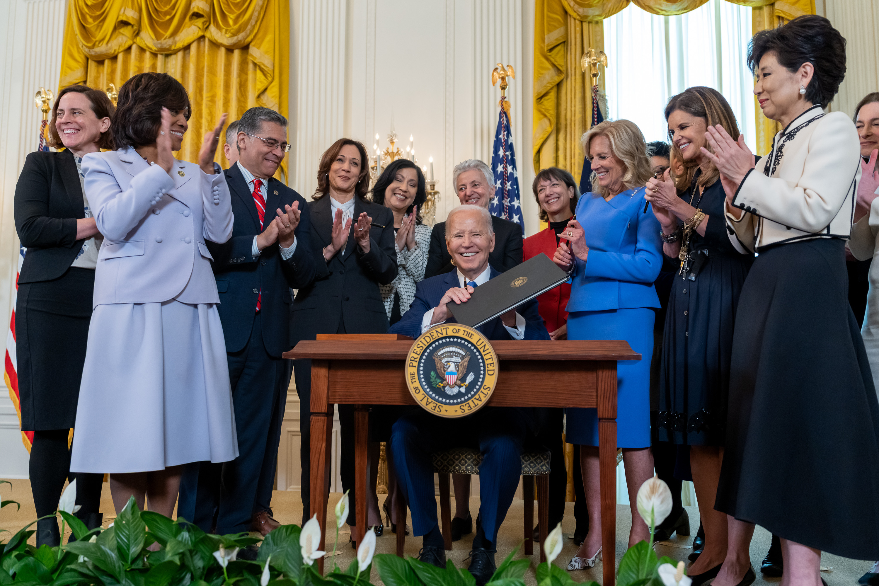 Photo of President Biden signing executive order surrounded by women in leadership clapping