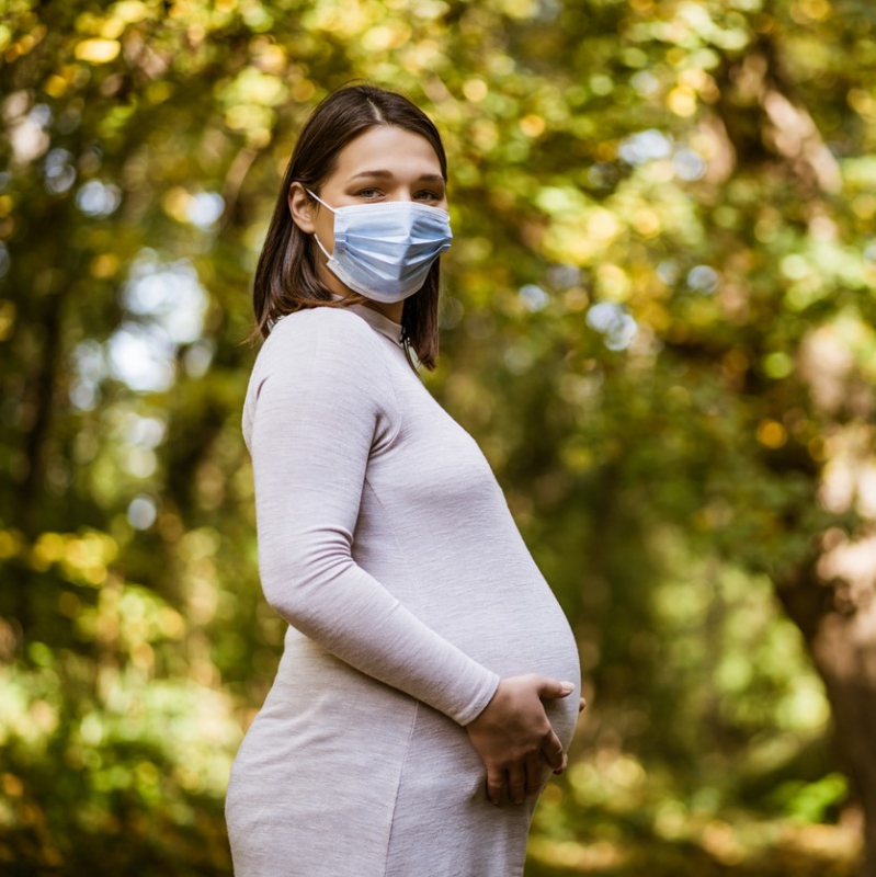Pregnant woman wearing a mask and holding her belly.