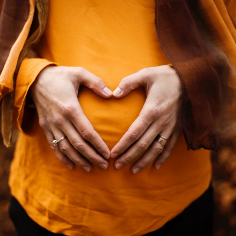 Pregnant woman holding her belly with her hands in a heart shape.