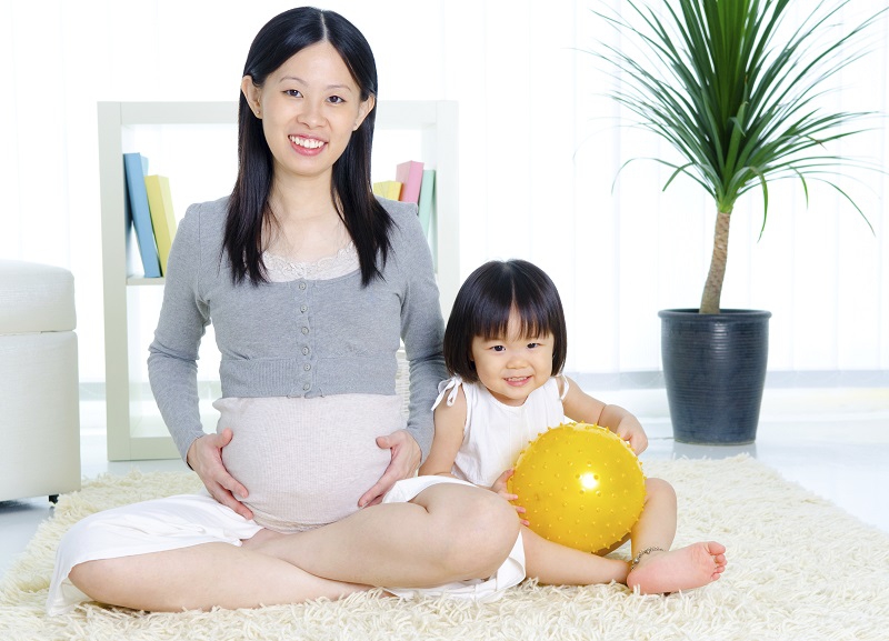 Smiling pregnant Asian woman with her daughter.