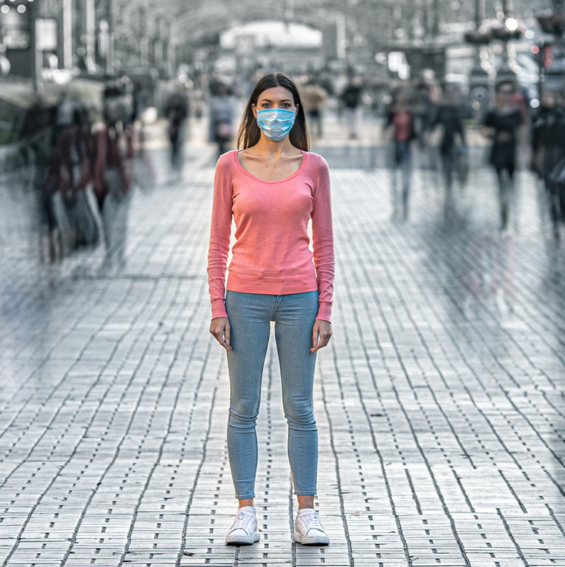 Woman wearing a mask to protect from COVID in the middle of a busy intersection.